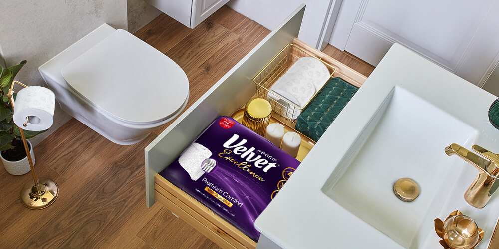 Widok z góry na szufladę łazienkową ze złotymi dodatkami. W szufladzie leży opakowanie papieru toaletowego Velvet Excellence Premium Comfort.